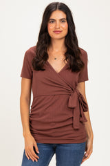 woman wearing a rust-colored short sleeve wrap top with a tie detail at the waist and jeans