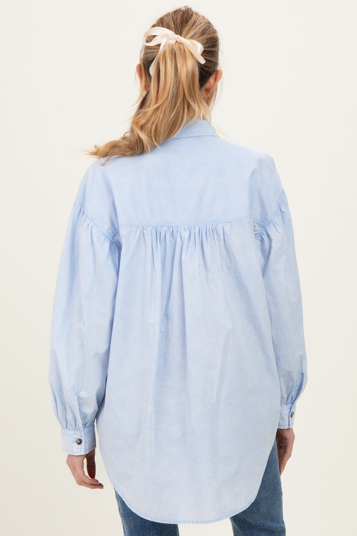 woman wearing a light blue maternity shirt with a relaxed fit and puffed sleeves, showing the back view