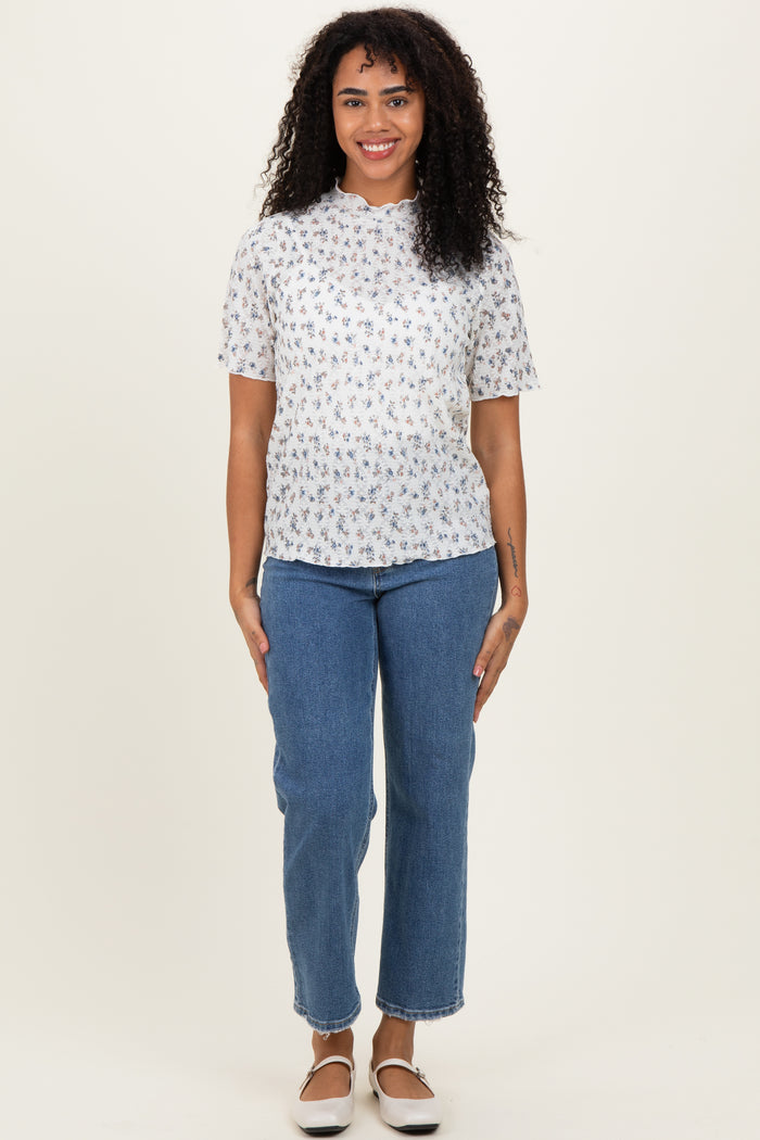 woman wearing a white short sleeve floral print top and blue high-waisted jeans standing against a neutral background