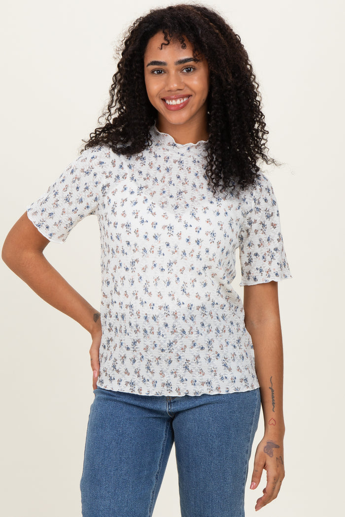 woman wearing a white floral short sleeve top with a scalloped neckline and smiling