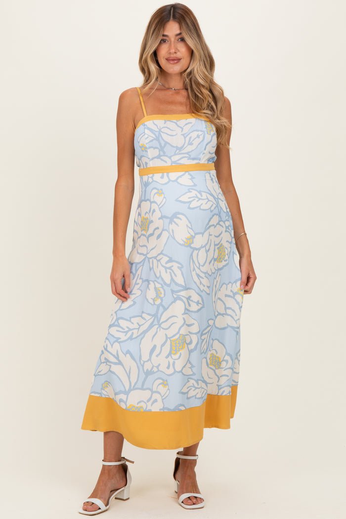 woman wearing a light blue floral maternity dress with yellow accents and a fitted bodice, showcasing her baby bump