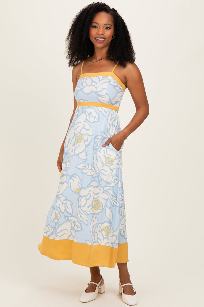 woman wearing a light blue floral maxi dress with yellow accents and pockets, standing against a plain background