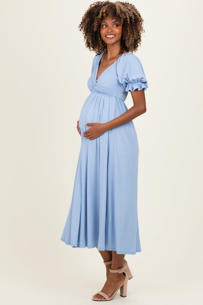 woman wearing a light blue maternity dress with short puff sleeves and a twisted front detail, showing her baby bump