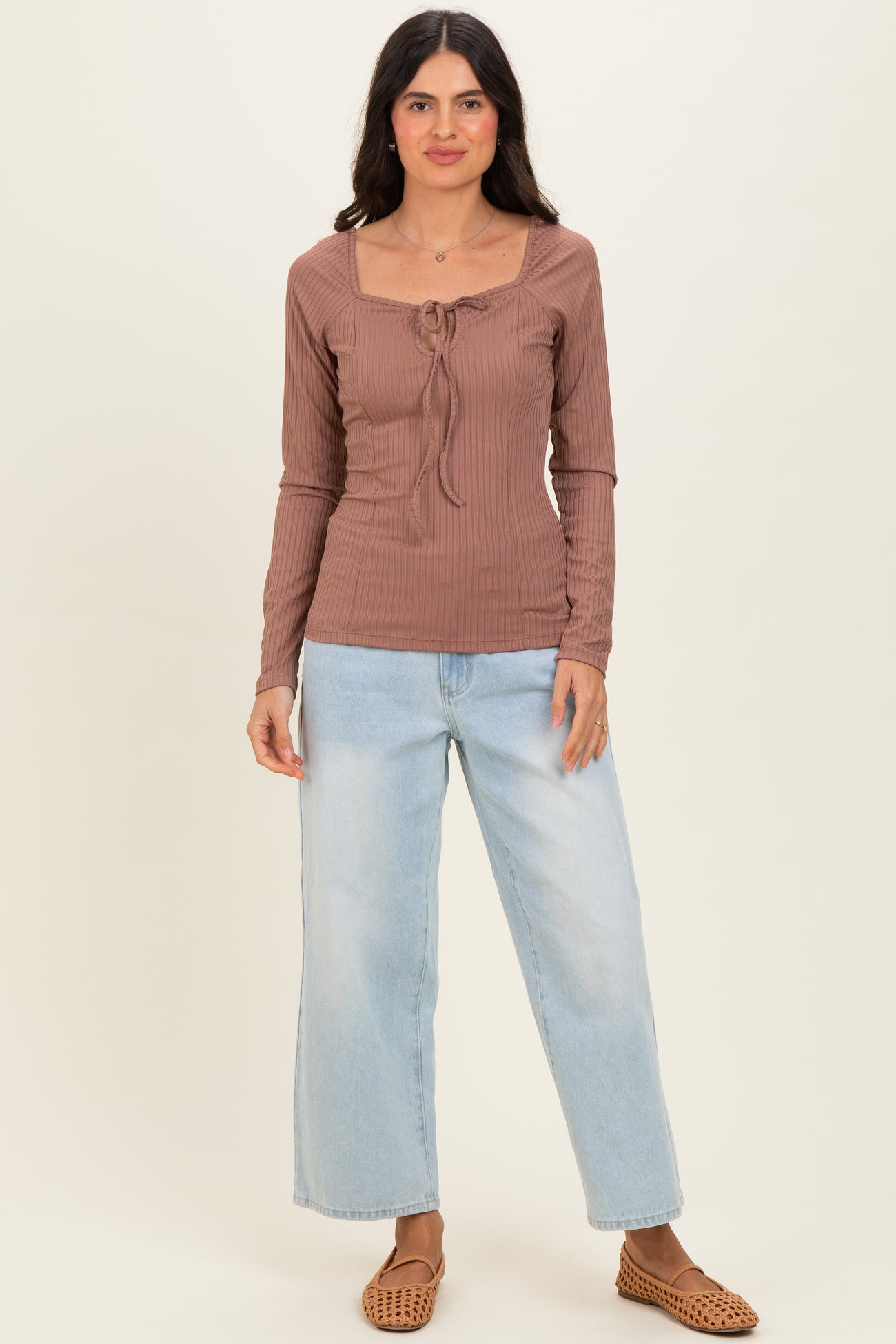 woman wearing a brown ribbed long sleeve top with a square neckline and tie detail, paired with light blue wide-leg jeans