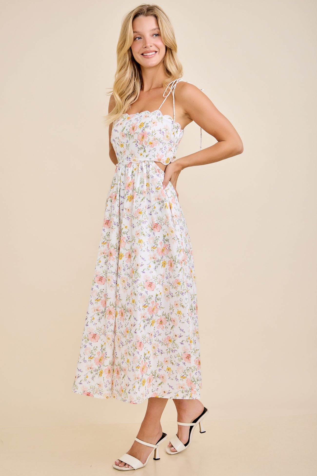 woman wearing a floral midi dress with spaghetti straps and a fitted bodice, standing in a light pose on a neutral background