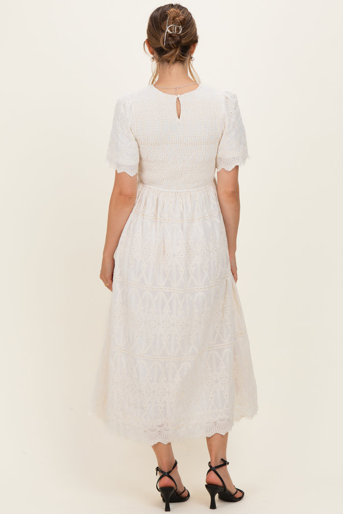 woman wearing a white maternity dress with short puff sleeves and a keyhole back, showing off a baby bump