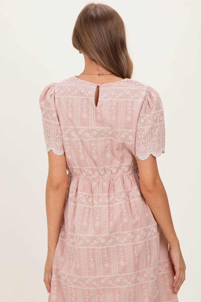 woman wearing a pink maternity dress with puff sleeves and lace detailing, showing the back view