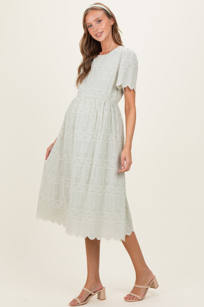 woman wearing a light green embroidered maternity dress with flutter sleeves and a cinched waist, showcasing her baby bump