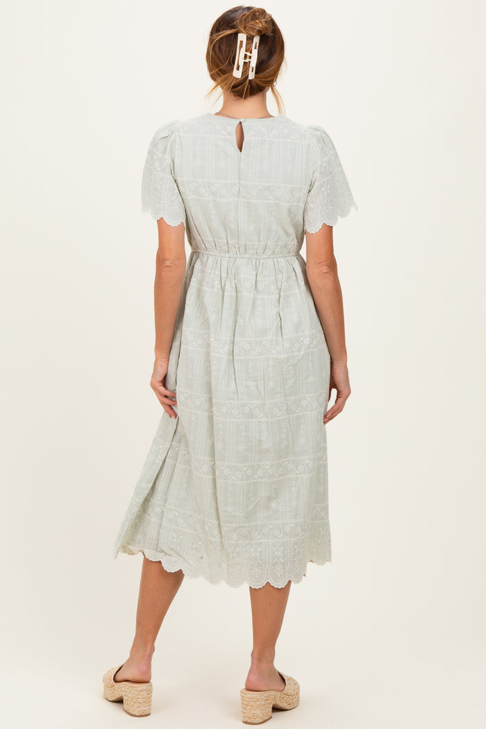 woman wearing a light green midi dress with short sleeves and lace detailing, showing a back keyhole and elastic waist