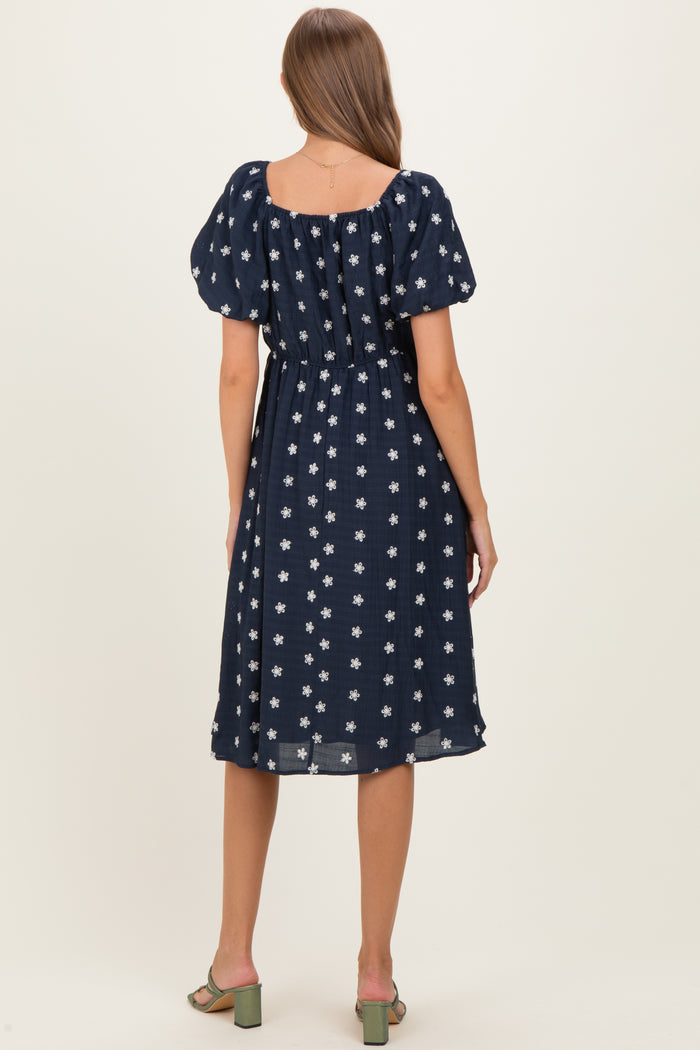 woman wearing a navy blue maternity dress with white floral pattern and puff sleeves, seen from the back