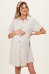 woman wearing a beige short sleeve maternity dress with button details and holding her baby bump