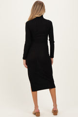 woman wearing a black ribbed maternity dress with long sleeves and a back slit, showcasing her baby bump