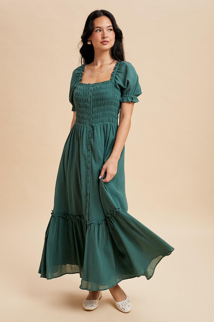 woman wearing a green smocked maxi dress with puff sleeves and ruffles, standing against a beige background