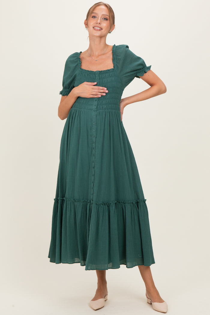 woman wearing a dark green maternity dress with puff sleeves and a tiered skirt, holding her baby bump.