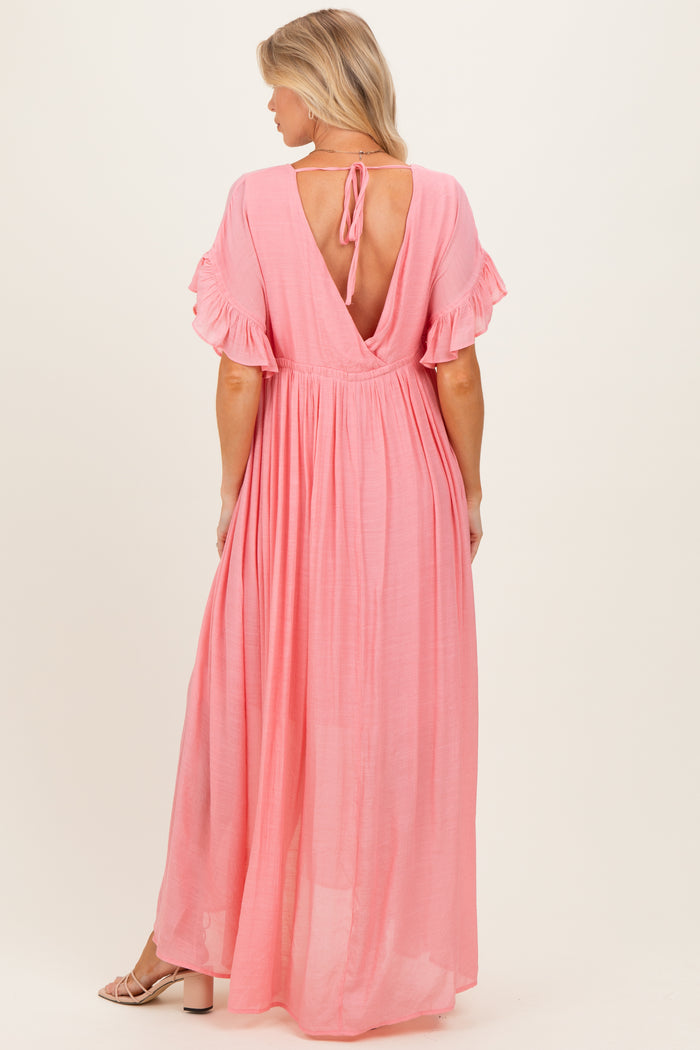 woman wearing a pink backless maxi maternity dress with ruffle sleeves and a tie at the neck