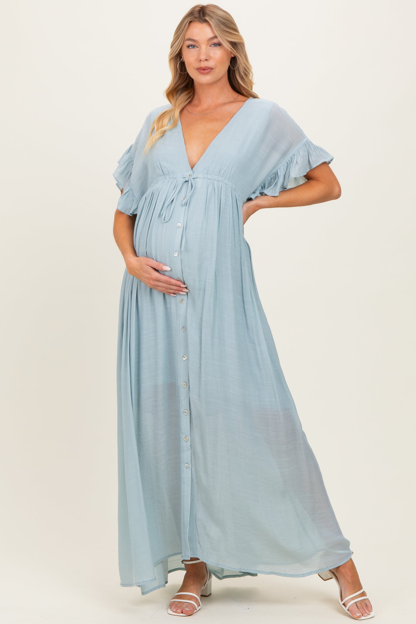 woman wearing a light blue maternity maxi dress with ruffled sleeves and a button-down front, gently holding her baby bump