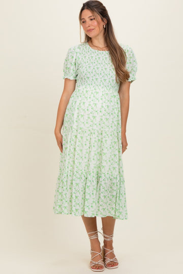 woman wearing a green floral maternity dress with short puff sleeves and a tiered skirt, showcasing her baby bump