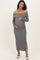 woman wearing a grey off-the-shoulder maternity dress with long sleeves and a side slit, holding her baby bump