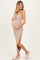 woman wearing a beige maternity dress with side slits, holding her baby bump and standing on a light background