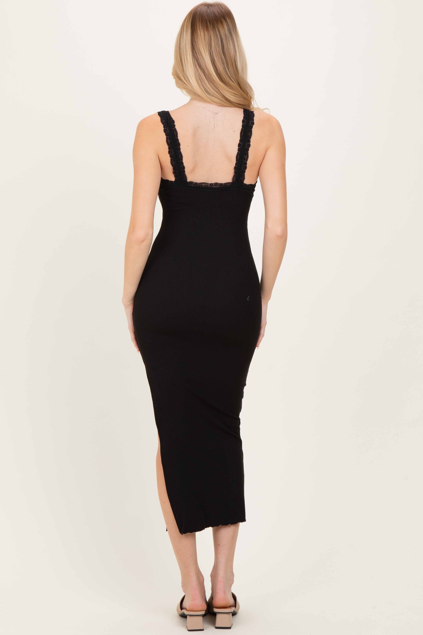 woman wearing a black ribbed midi dress with lace straps and a side slit, shown from the back