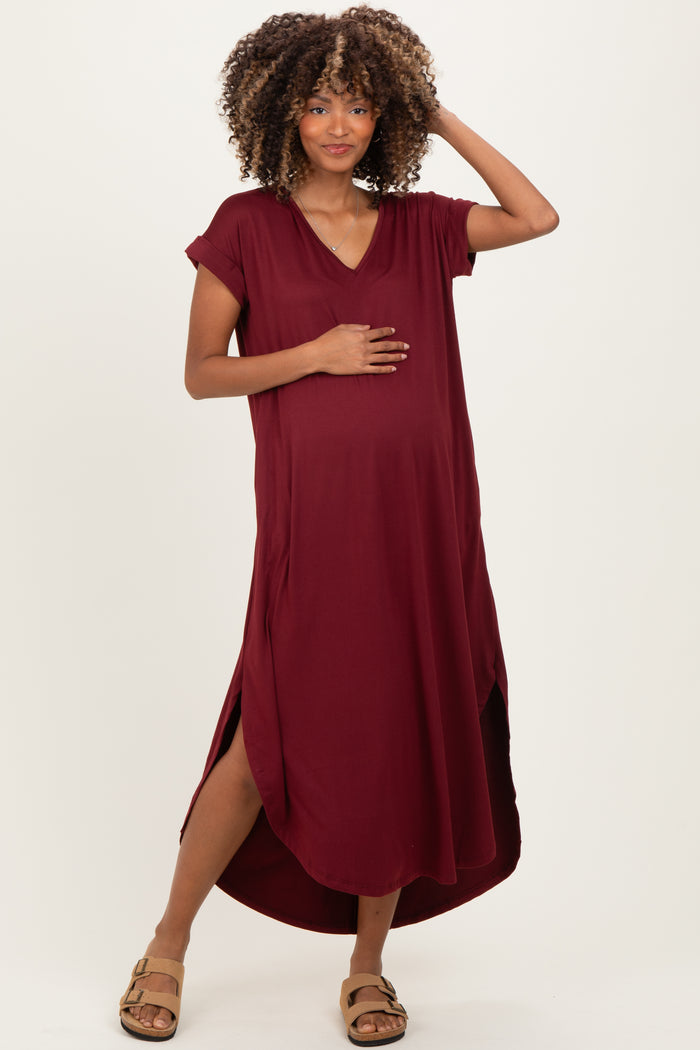 woman wearing a maroon maternity dress with short sleeves and side slits, holding her baby bump