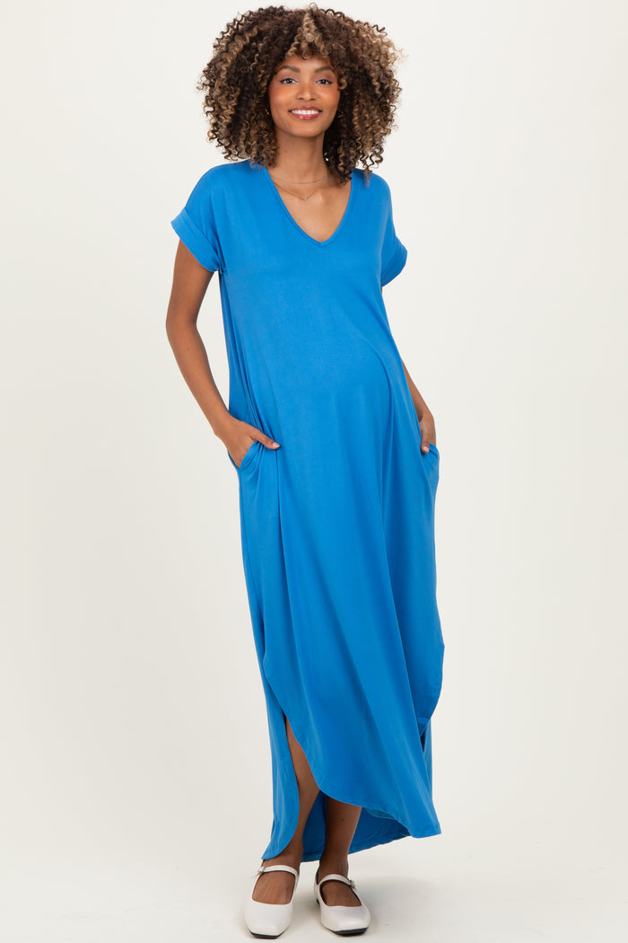 woman wearing a bright blue short sleeve maternity maxi dress with pockets and side slits, showcasing her baby bump