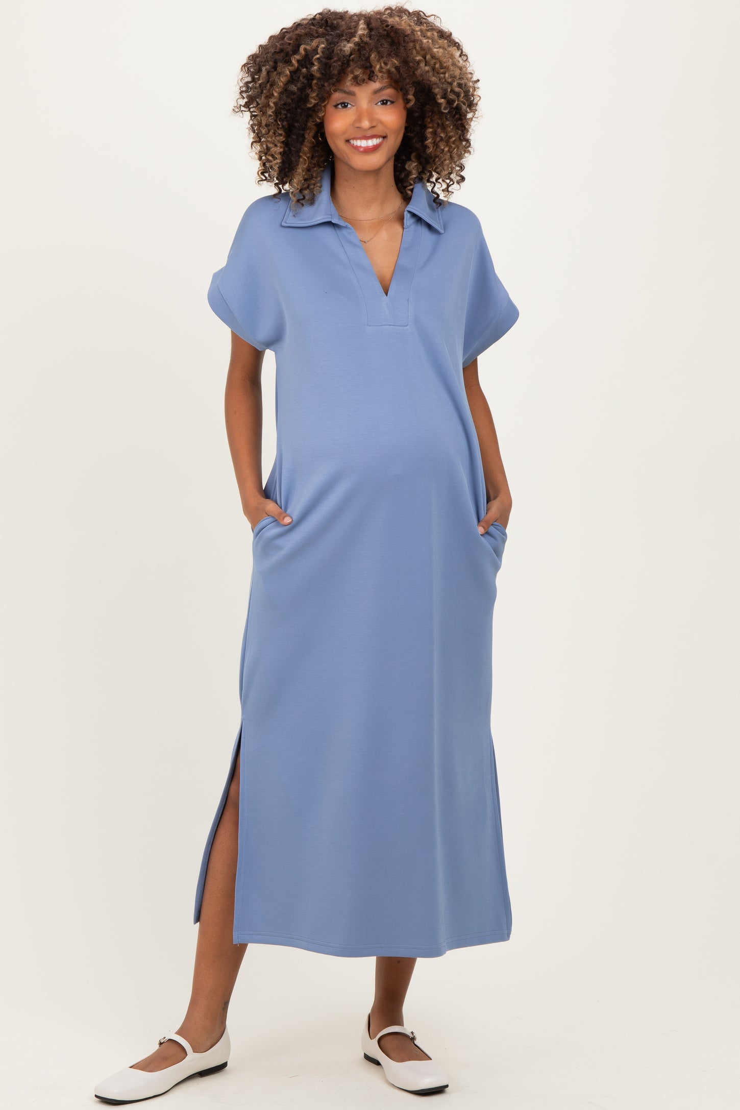 woman wearing a light blue maternity dress with a collared neckline and side pockets, showing off her baby bump