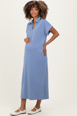woman wearing a light blue maternity midi dress with a polo collar and side pockets, gently holding her baby bump