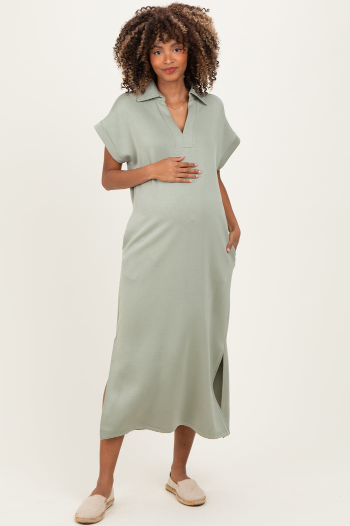woman wearing a sage green maternity dress with short sleeves and side slits, holding her baby bump
