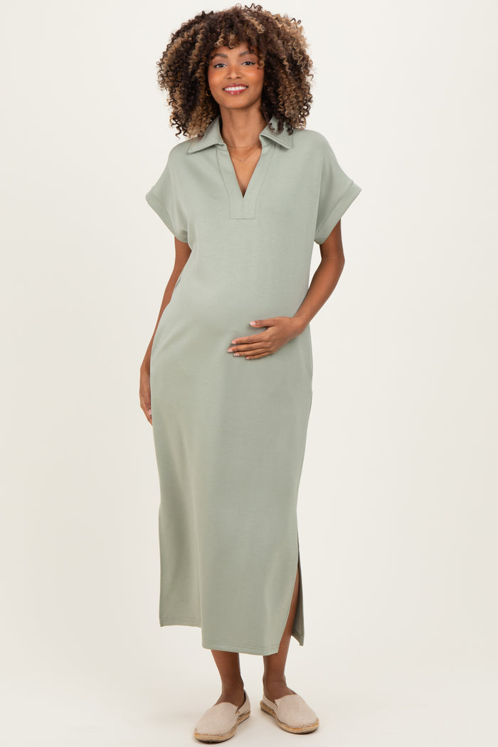 woman wearing a sage green maternity maxi dress with a polo collar and side slits, holding her baby bump