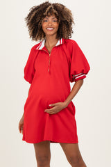 woman wearing a red maternity dress with a half-zip front and striped collar, holding her baby bump