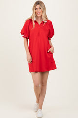 woman wearing a red short sleeve polo dress with a zip neckline and puff sleeves, standing with one hand in the pocket