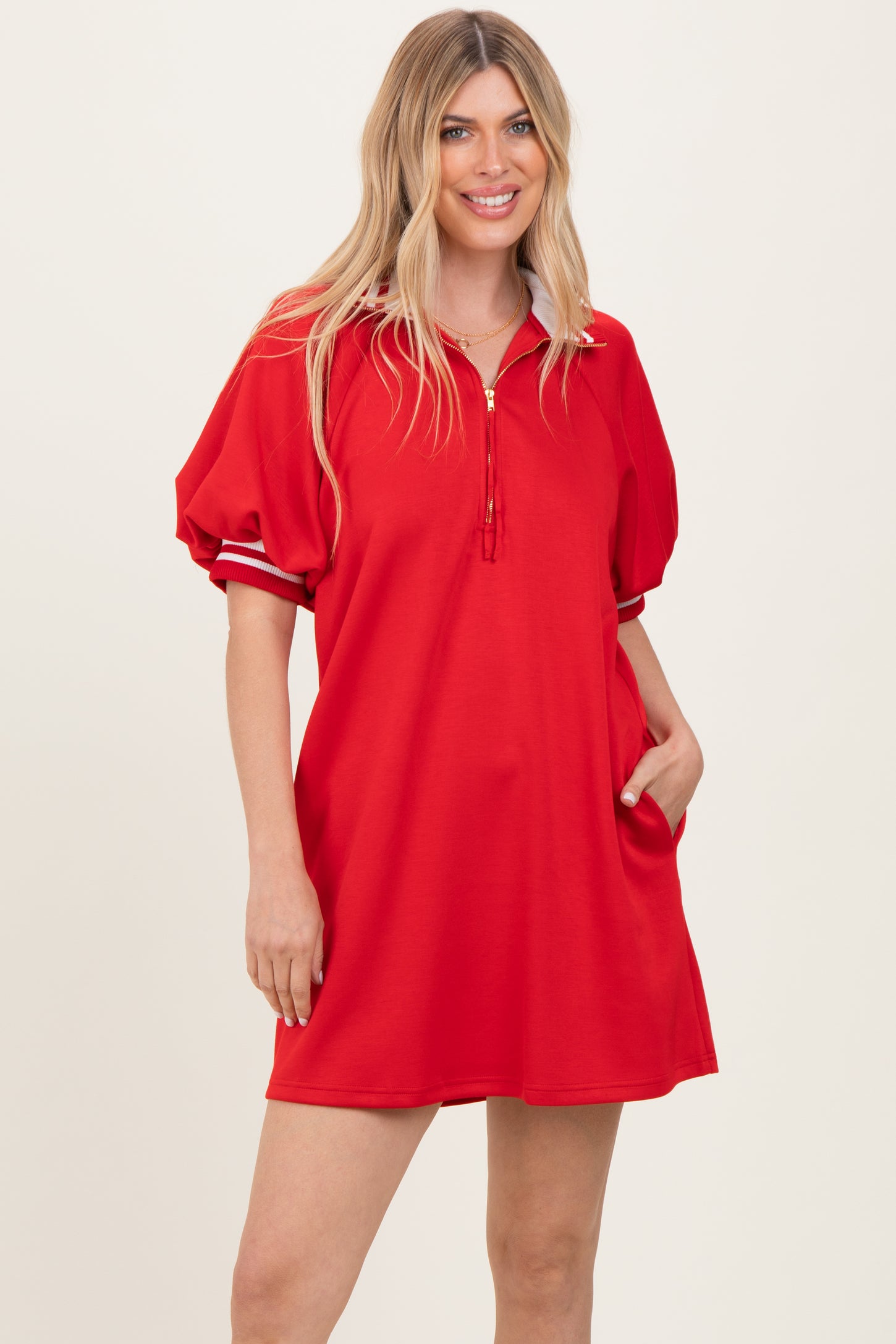 woman wearing a red short sleeve polo dress with puff sleeves and a zipper detail at the neck, standing with one hand in her pocket