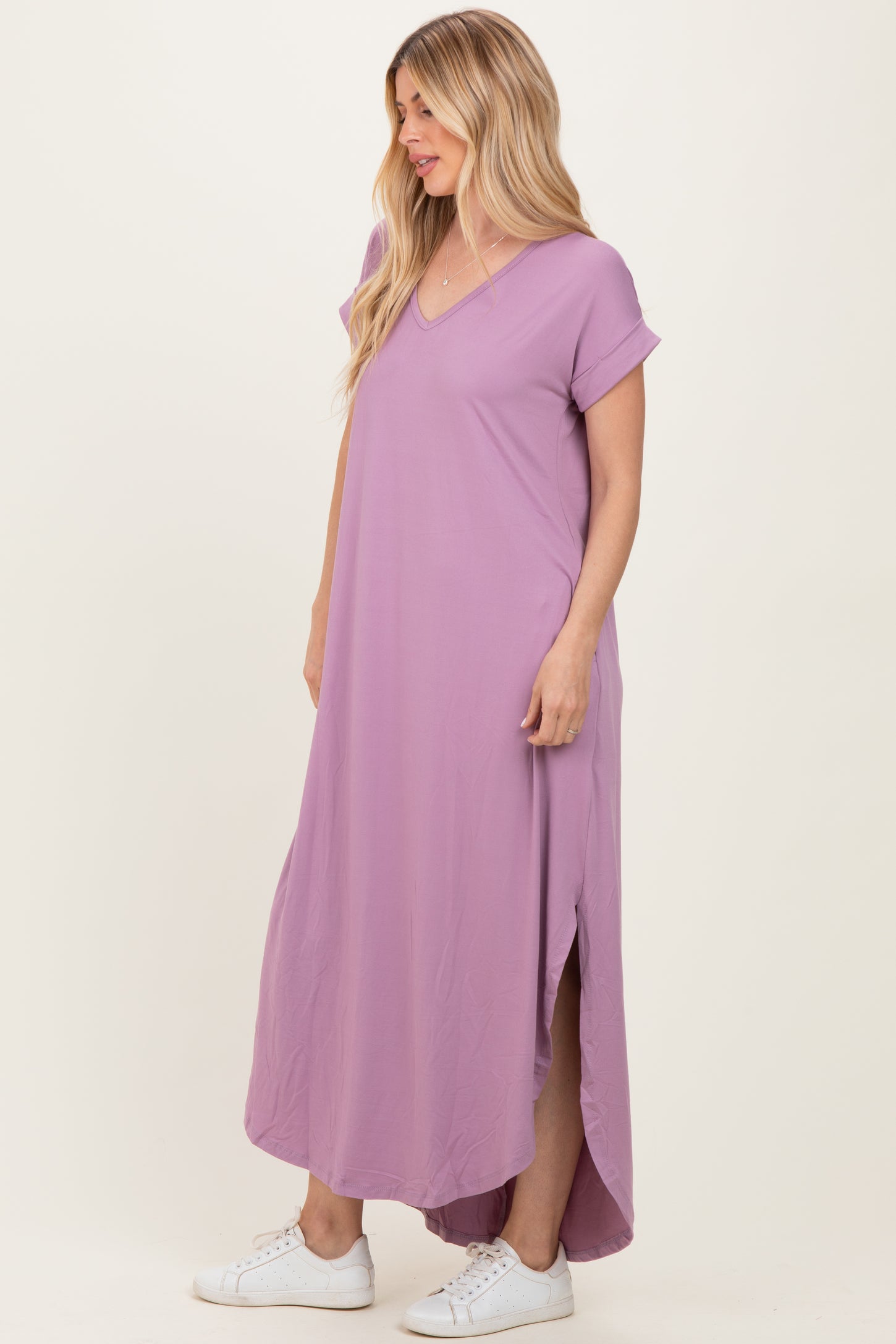 woman wearing a pastel purple short sleeve maxi dress with a v-neck and side slits, styled with white sneakers