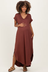 woman wearing a rust brown maternity maxi dress with short sleeves and side slits, gently cradling her baby bump