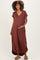woman wearing a rust-colored maternity maxi dress, smiling and holding her baby bump