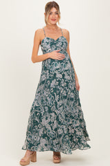 woman wearing a green floral maxi maternity dress and holding her baby bump