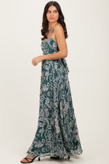 woman wearing a flowy green maxi dress with a floral pattern and spaghetti straps, styled with strappy black heels