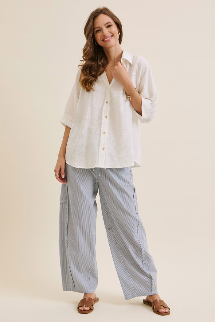 woman wearing a white button-up oversized shirt and striped wide-leg pants with sandals