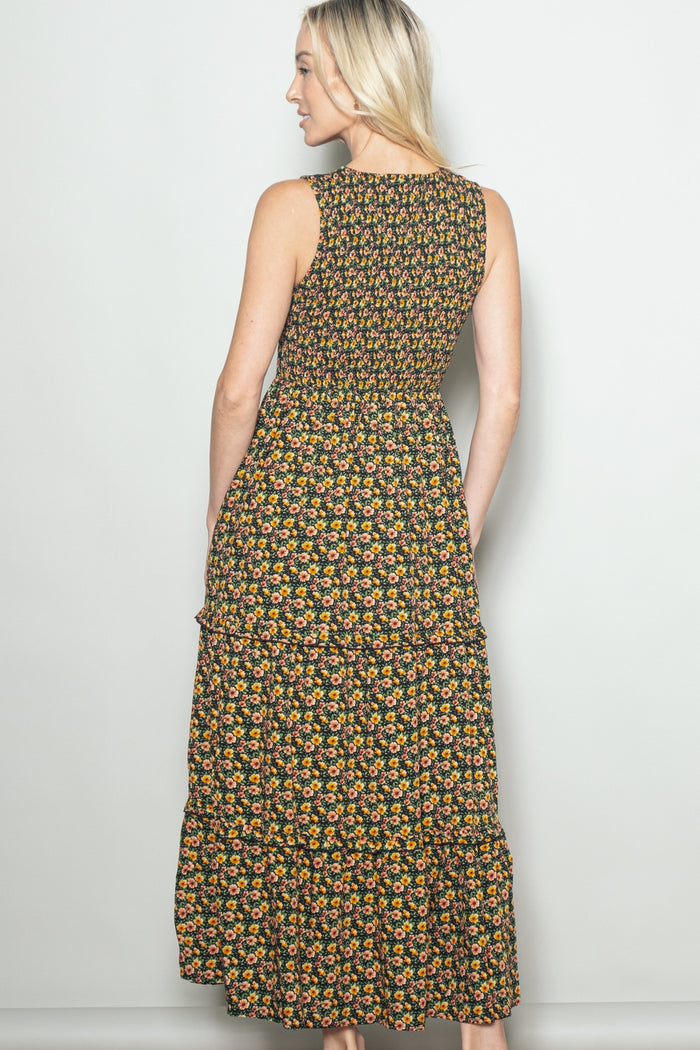 woman wearing a floral print black maxi dress with a tiered skirt and a fitted bodice, viewed from the back