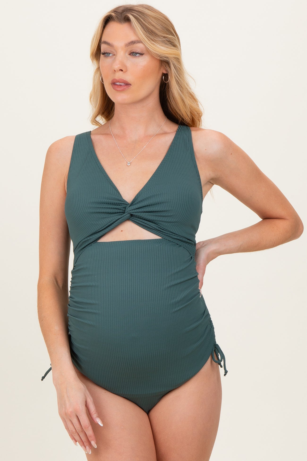 woman wearing a dark green maternity swimsuit with a twisted front and adjustable side ties, showcasing a baby bump