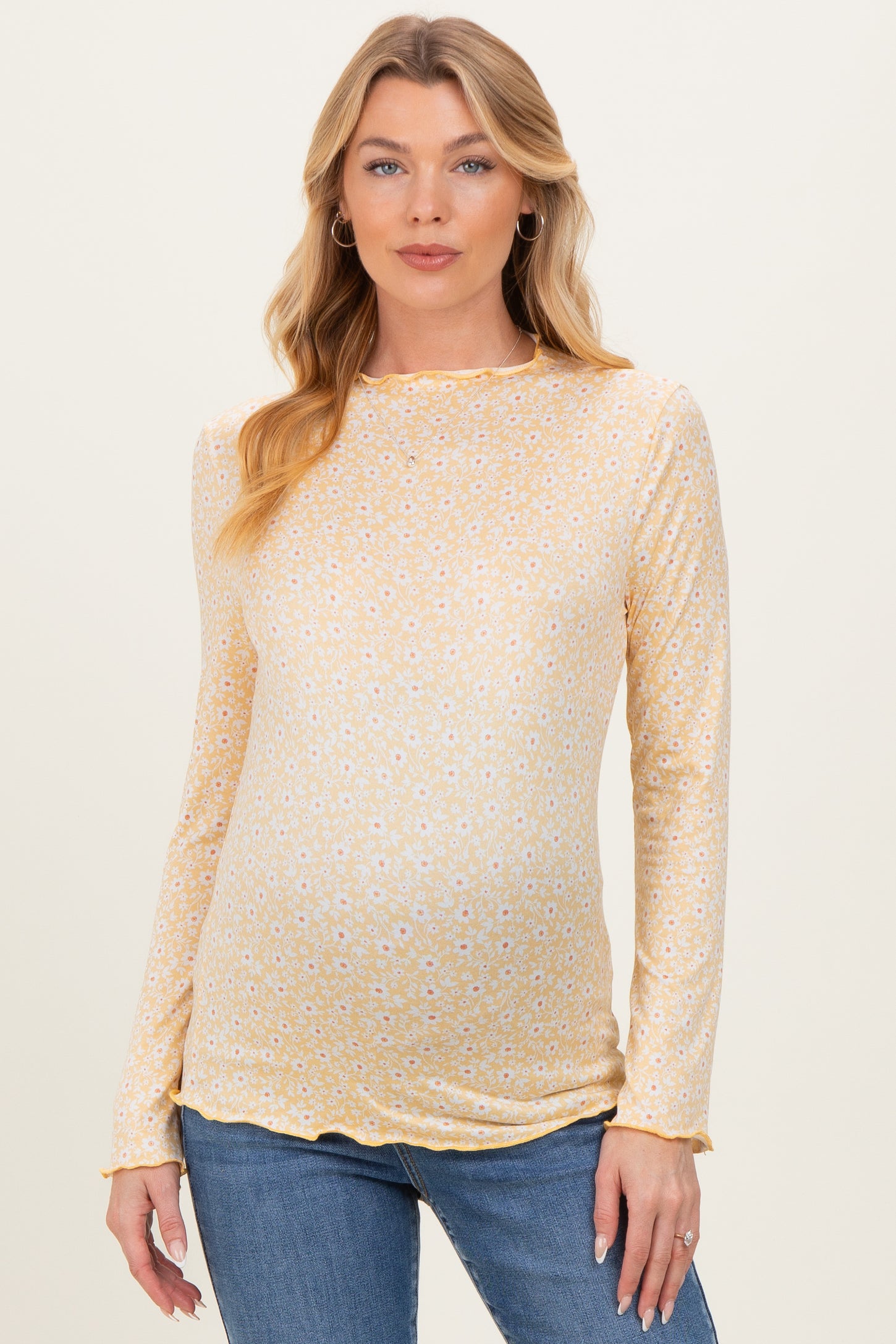woman wearing a yellow floral long sleeve maternity top and displaying her baby bump