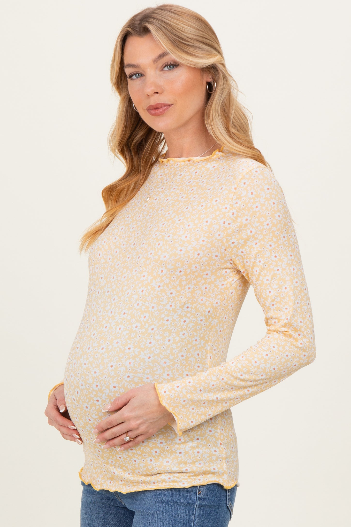 woman wearing a yellow long sleeve maternity top with floral print and holding her baby bump