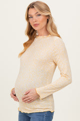 woman wearing a yellow long sleeve maternity top with floral print and holding her baby bump