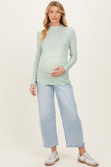 woman wearing a green floral long sleeve maternity top and light blue wide leg jeans, holding her baby bump