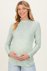woman wearing a light green floral long sleeve maternity top and holding her baby bump