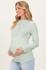 woman wearing a light green long sleeve maternity top with floral print and holding her baby bump