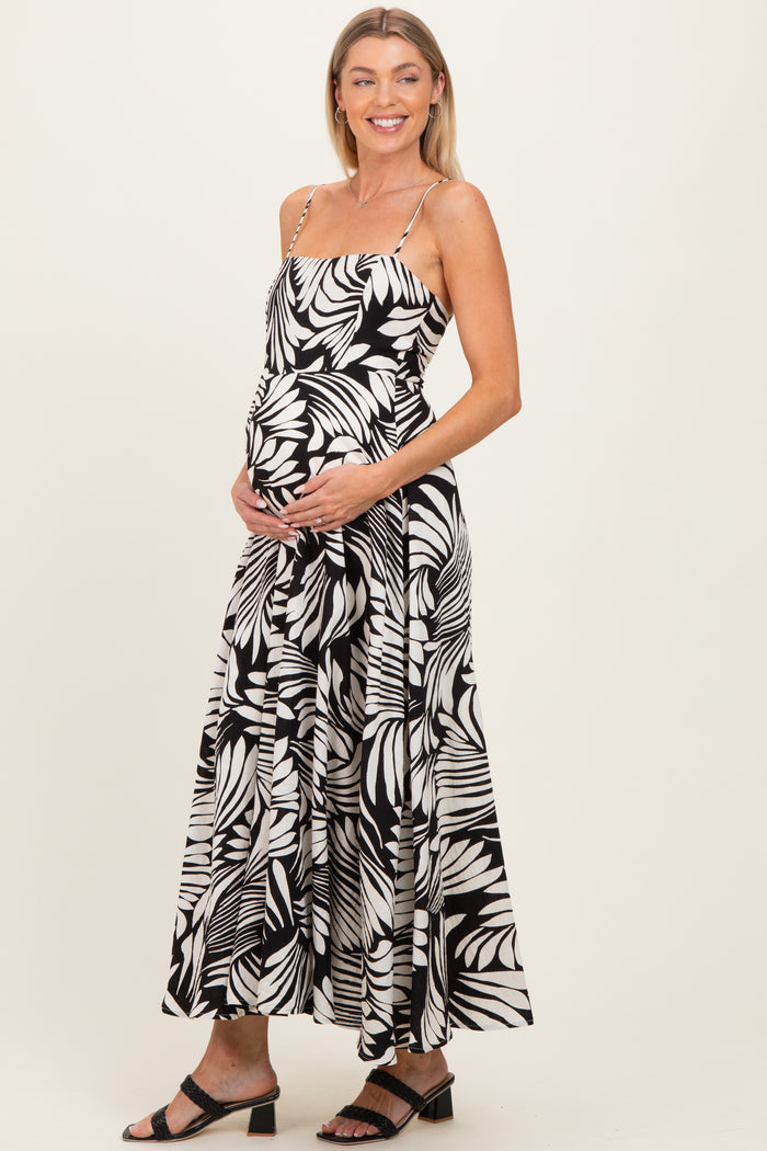 woman wearing a black and white floral print maternity dress with spaghetti straps and holding her baby bump