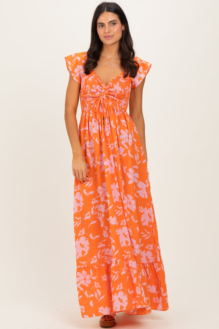 woman wearing an orange floral maxi dress with cap sleeves and a ruched bodice