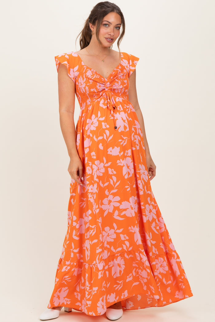 woman wearing an orange floral maternity maxi dress with ruffled sleeves and a tie waist detail, showing her baby bump